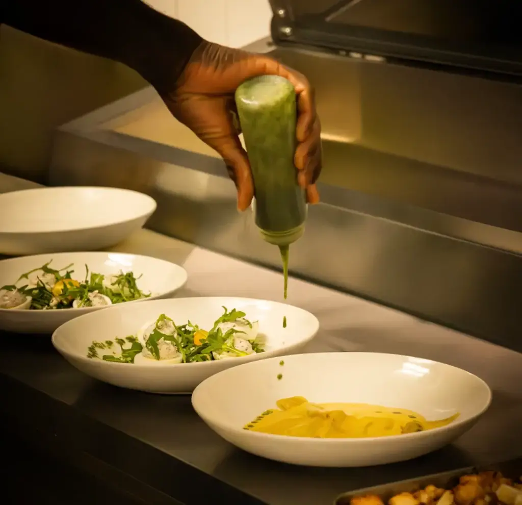 Chef de Madie dressant une assiette avec une sauce verte en cuisine.