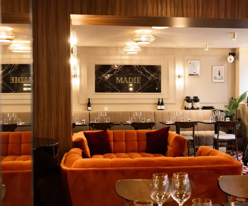 Intérieur du restaurant Madie avec canapé orangé, banquettes élégantes et logo MADIE au mur.
