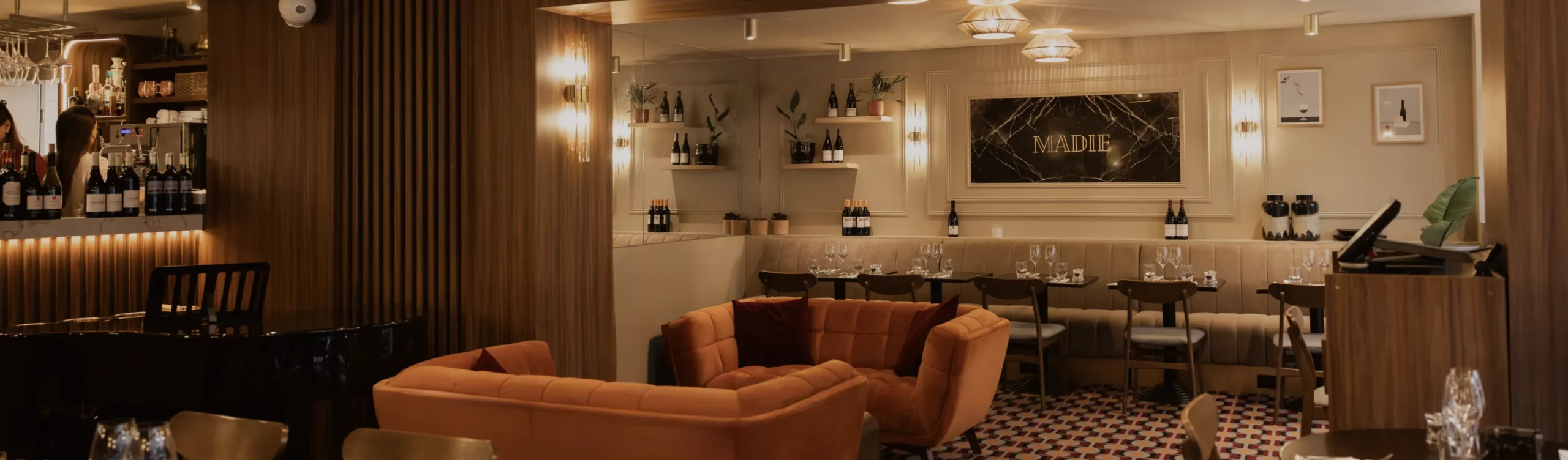 Intérieur du restaurant Madie à Paris 8, avec banquettes beiges, fauteuils orangés et ambiance chaleureuse.